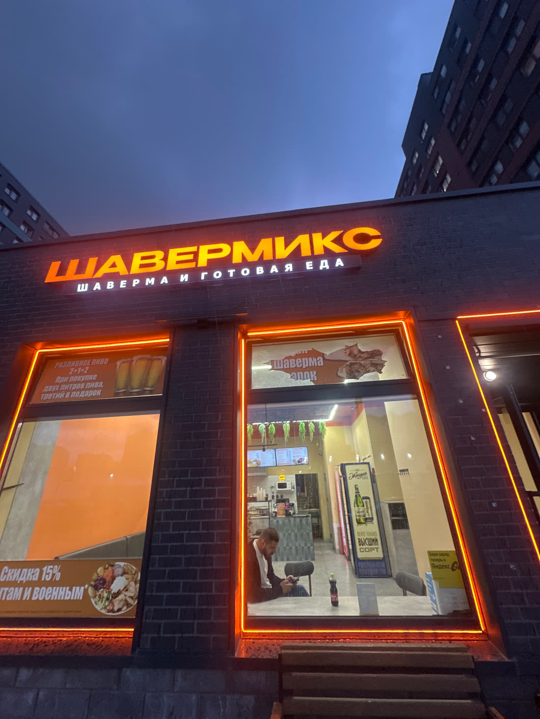 Фасад Шавермикса вечером: оранжевая вывеска, неон на окнах